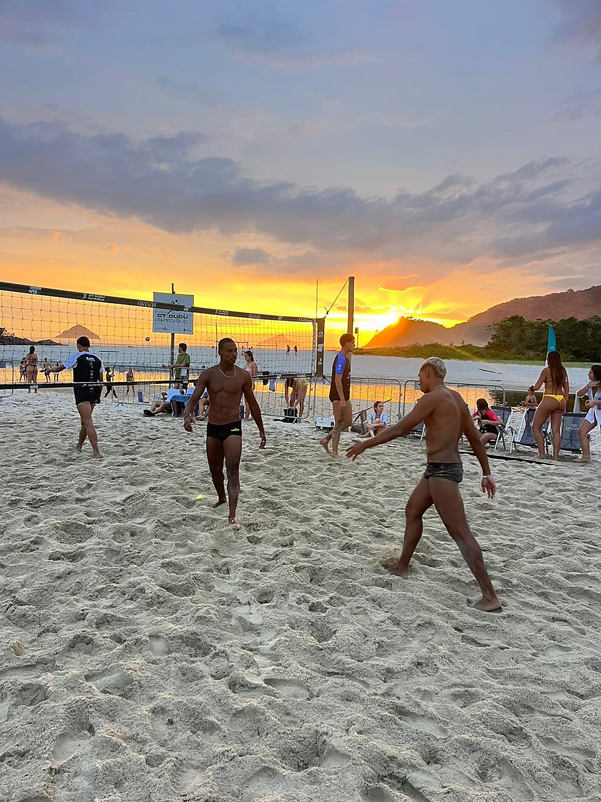 Atletas jogando futevôlei na areia ao entardecer no CT Dudu