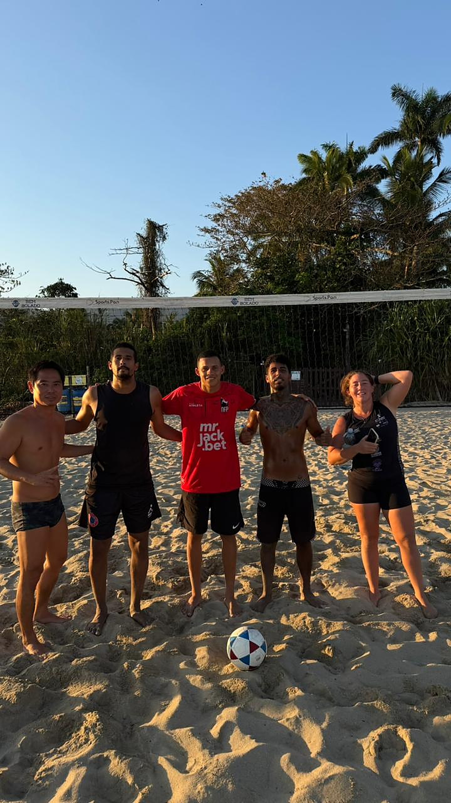Alunos do CT Dudu Futevôlei reunidos na quadra ao entardecer com a bola na areia